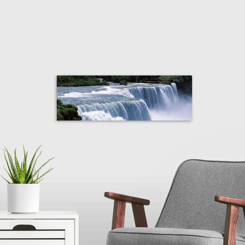 A modern room featuring A large panoramic photograph taken of Niagara falls with trees and foliage lining the back of the...