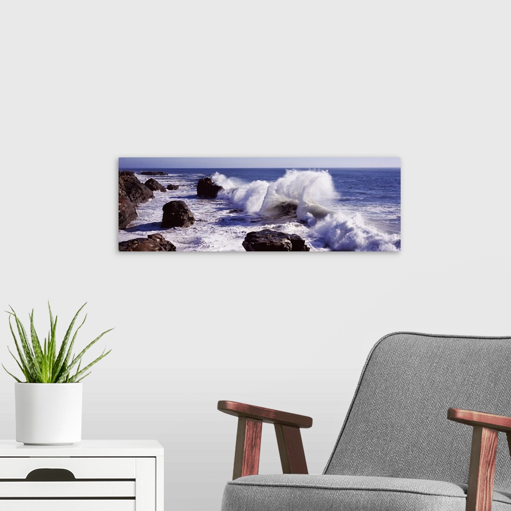 A modern room featuring Panoramic photograph of rock cliff line with large boulders and crashing waves under a clear sky.