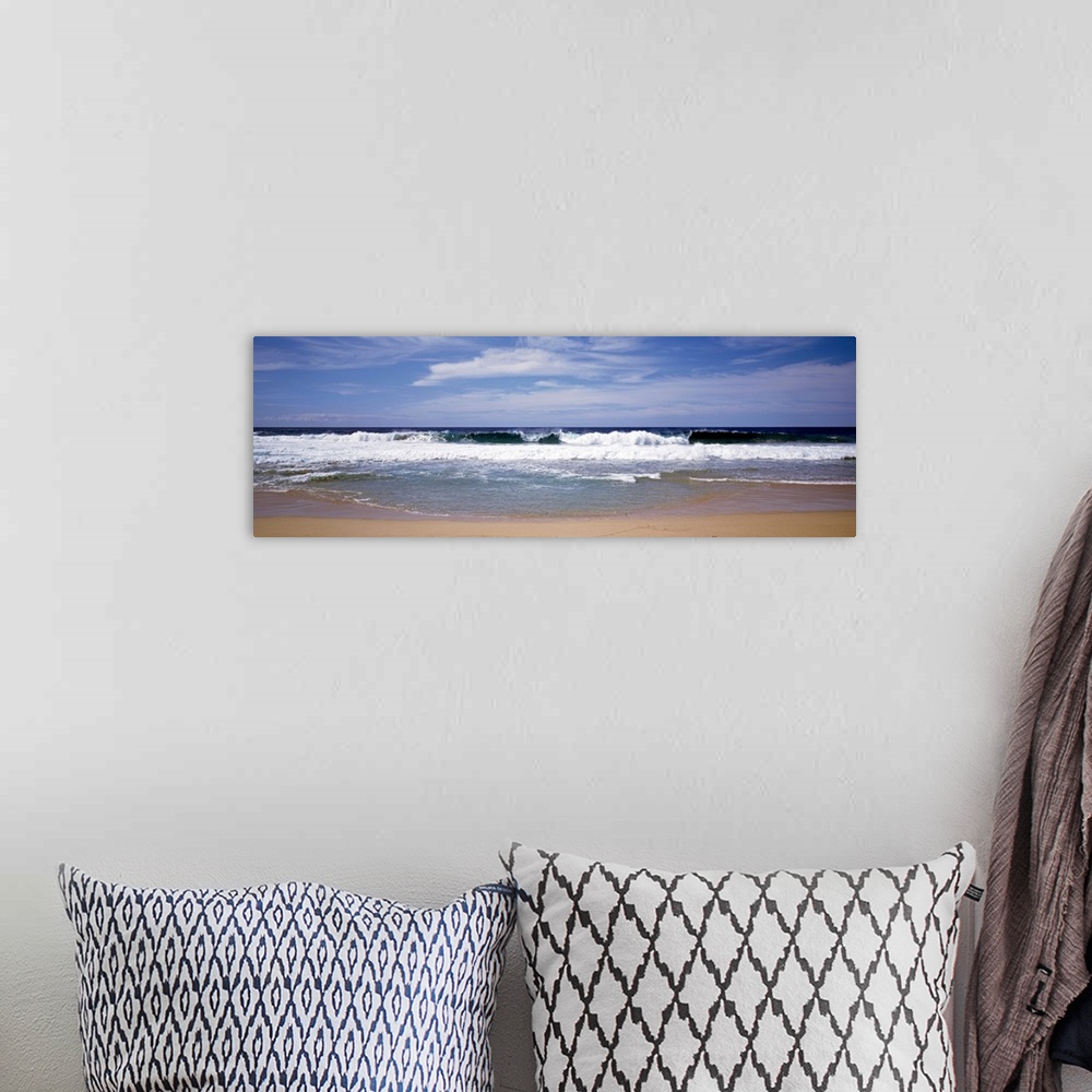 A bohemian room featuring Several clouds in the sky over crashing foamy waves on a sandy beach on the West Coast in a panor...