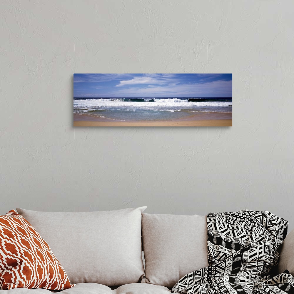 A bohemian room featuring Several clouds in the sky over crashing foamy waves on a sandy beach on the West Coast in a panor...