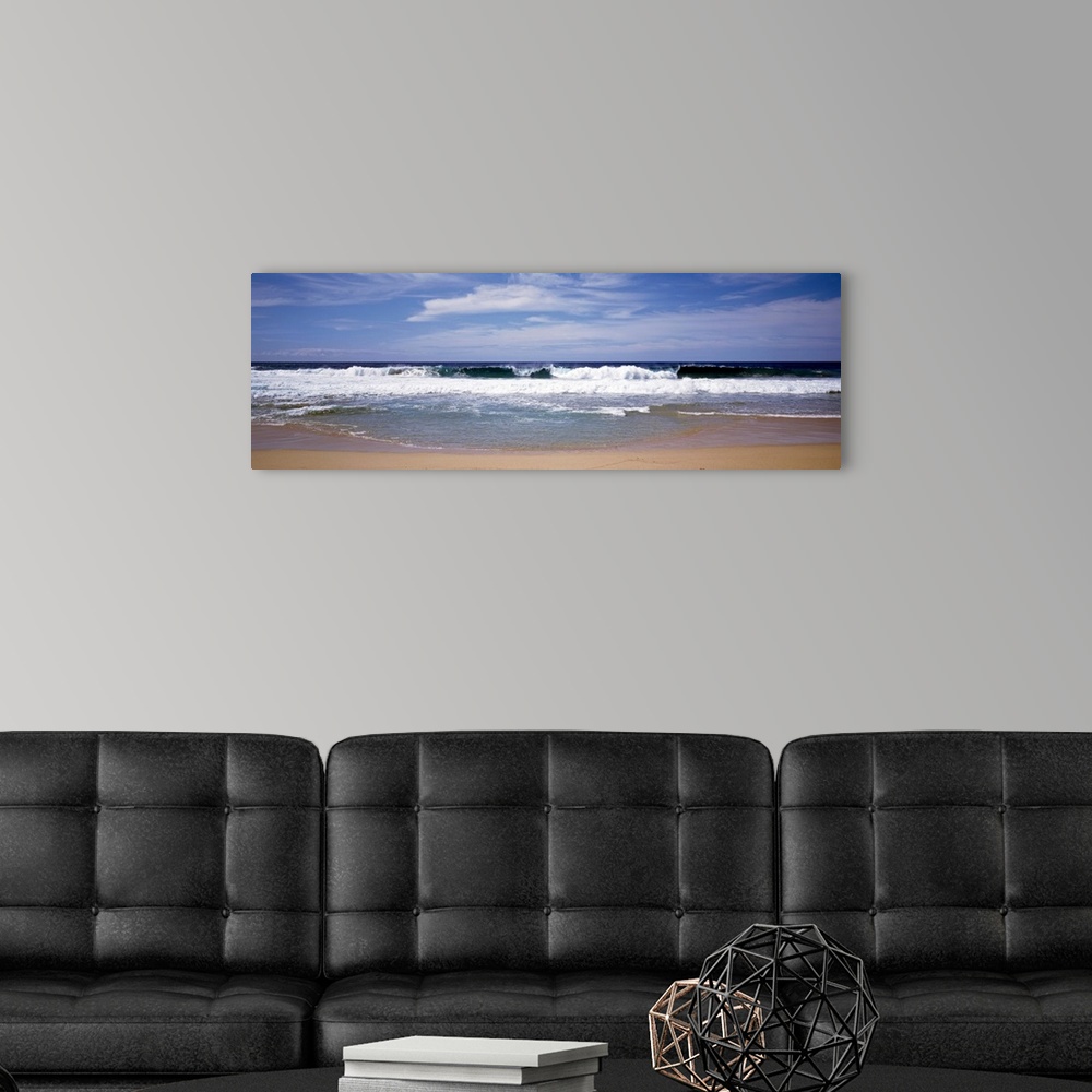 A modern room featuring Several clouds in the sky over crashing foamy waves on a sandy beach on the West Coast in a panor...