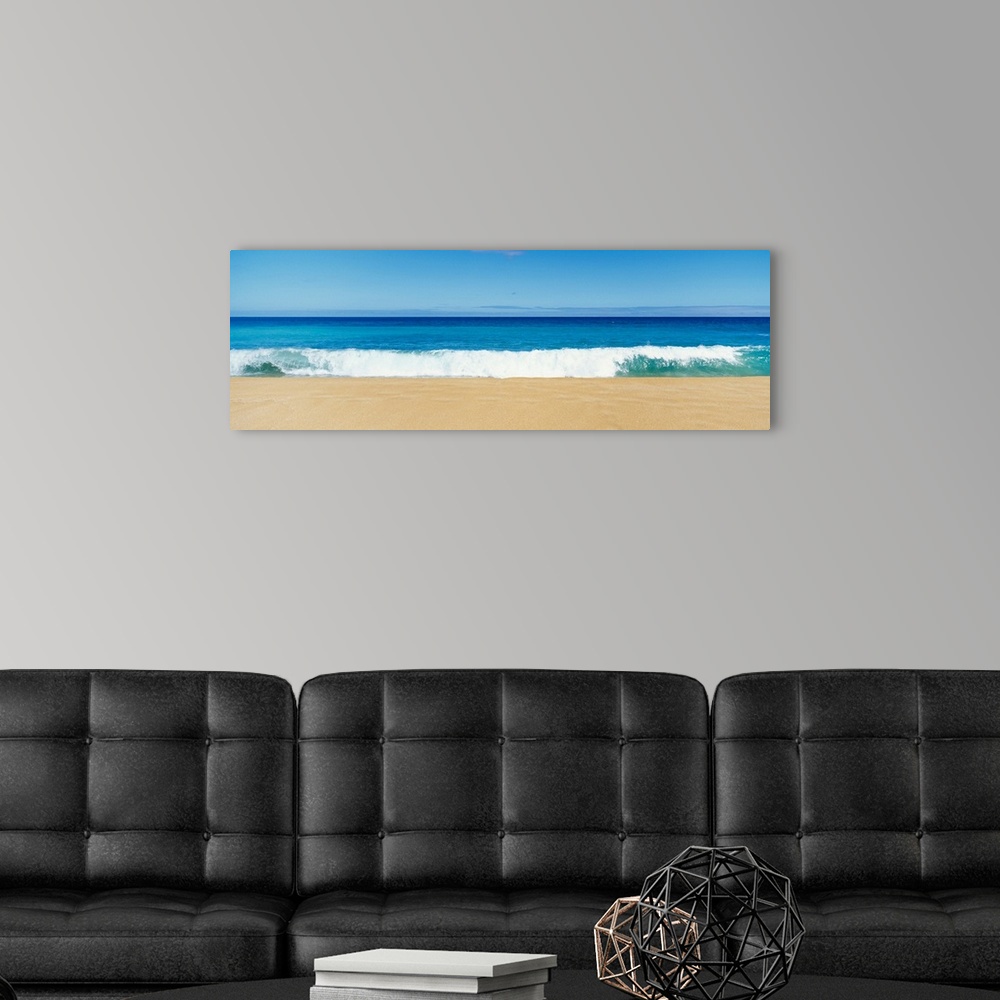 A modern room featuring This panoramic photograph captures a swell breaking on the sandy shore of a tropical beach on a c...
