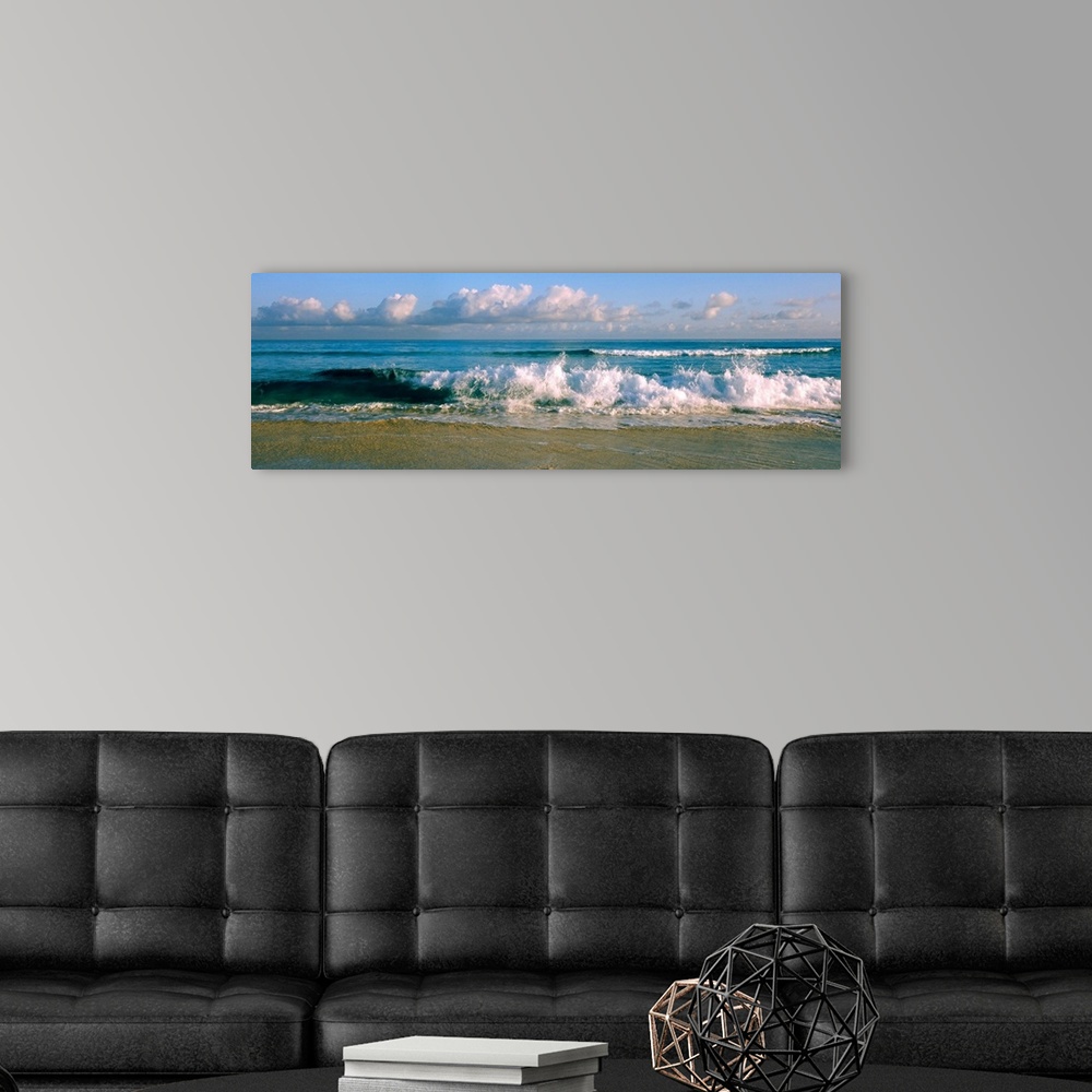 A modern room featuring Panoramic photograph of cloudy day at the beach with sea surf crashing onto the sand.