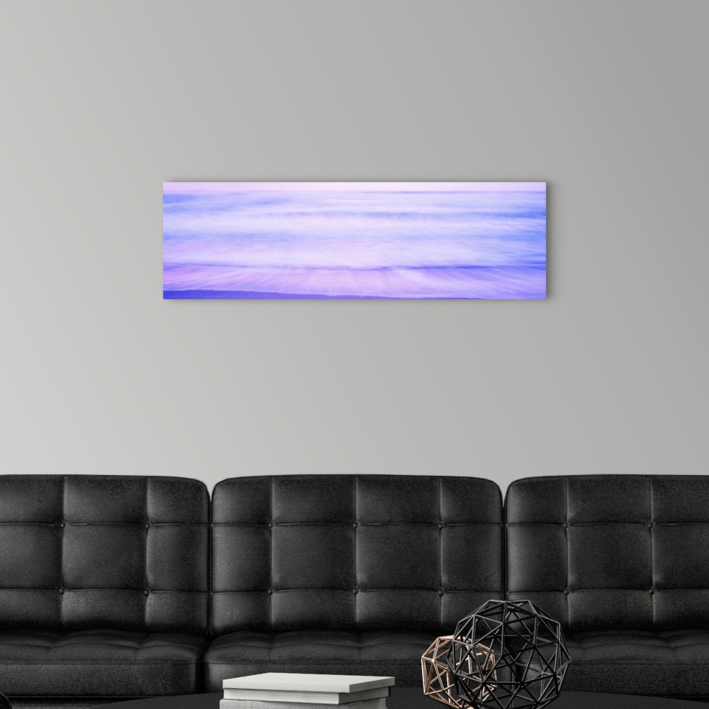 A modern room featuring A large panoramic picture taken of waves that are about to hit the beach with a dusk like sky abo...