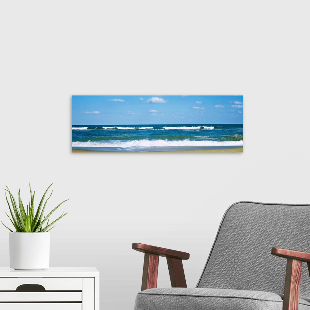 A modern room featuring Panoramic landscape photograph of a clear day at the beach with waves washing up on the sandy beach.