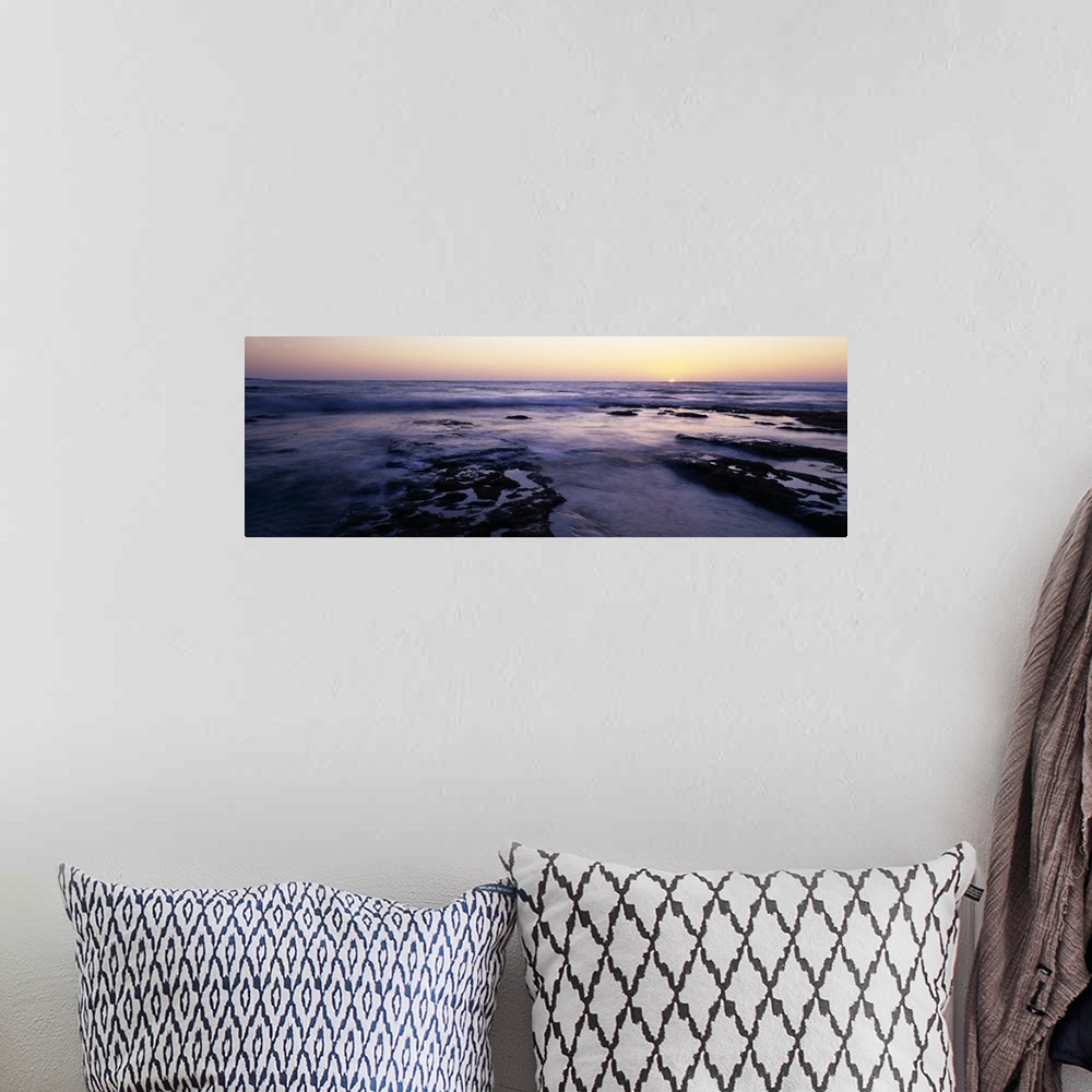 A bohemian room featuring Panoramic photograph taken of the ocean as the water flows over rocks and the sun is shown settin...