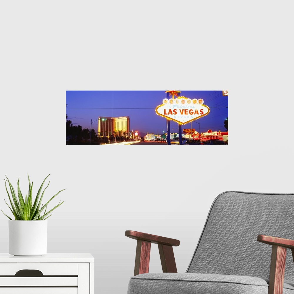 A modern room featuring Panoramic photograph of huge neon sign in ""Sin City"" with buildings lit up in the distance at d...