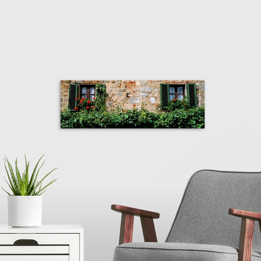 A modern room featuring Rustic masonry makes the wall of a house surrounded by overgrown hedges and enormous red flowers ...