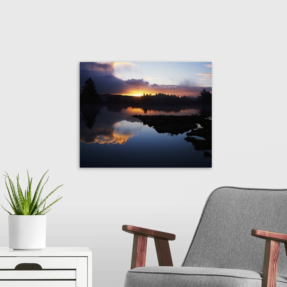 A modern room featuring Still lake reflecting the rising sun, clouds, and surrounding forest in the morning in Oregon.