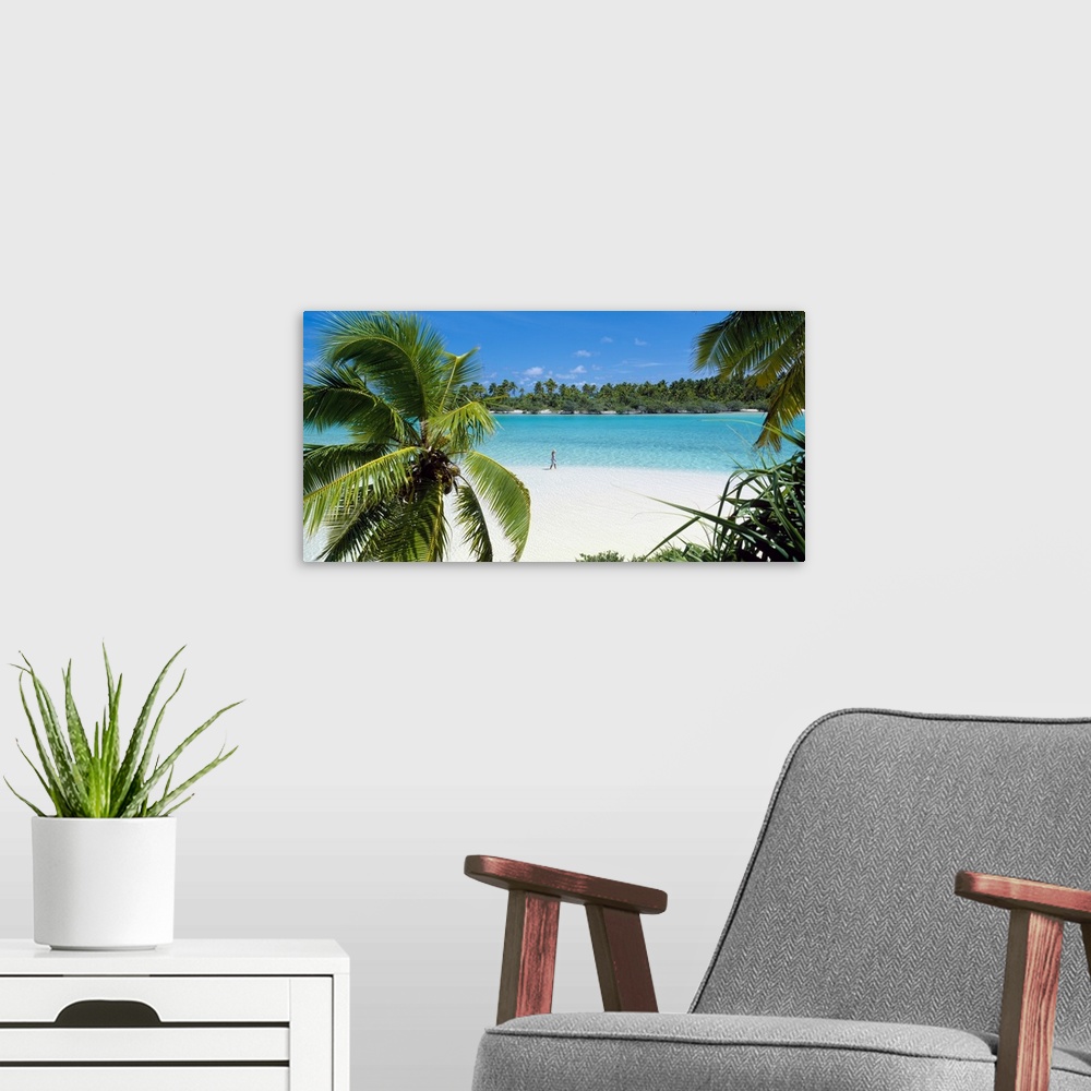 A modern room featuring Photograph of a lady walking alone on a white sand beach surrounded by crystal clear water and pa...