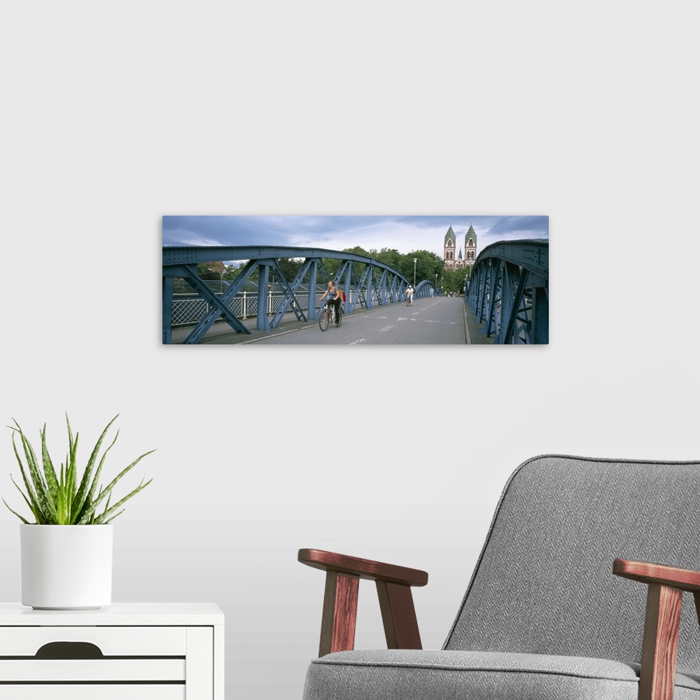 A modern room featuring Woman riding a bicycle on a bridge with a church in the background, Herz-Jesu Church, Freiburg Im...