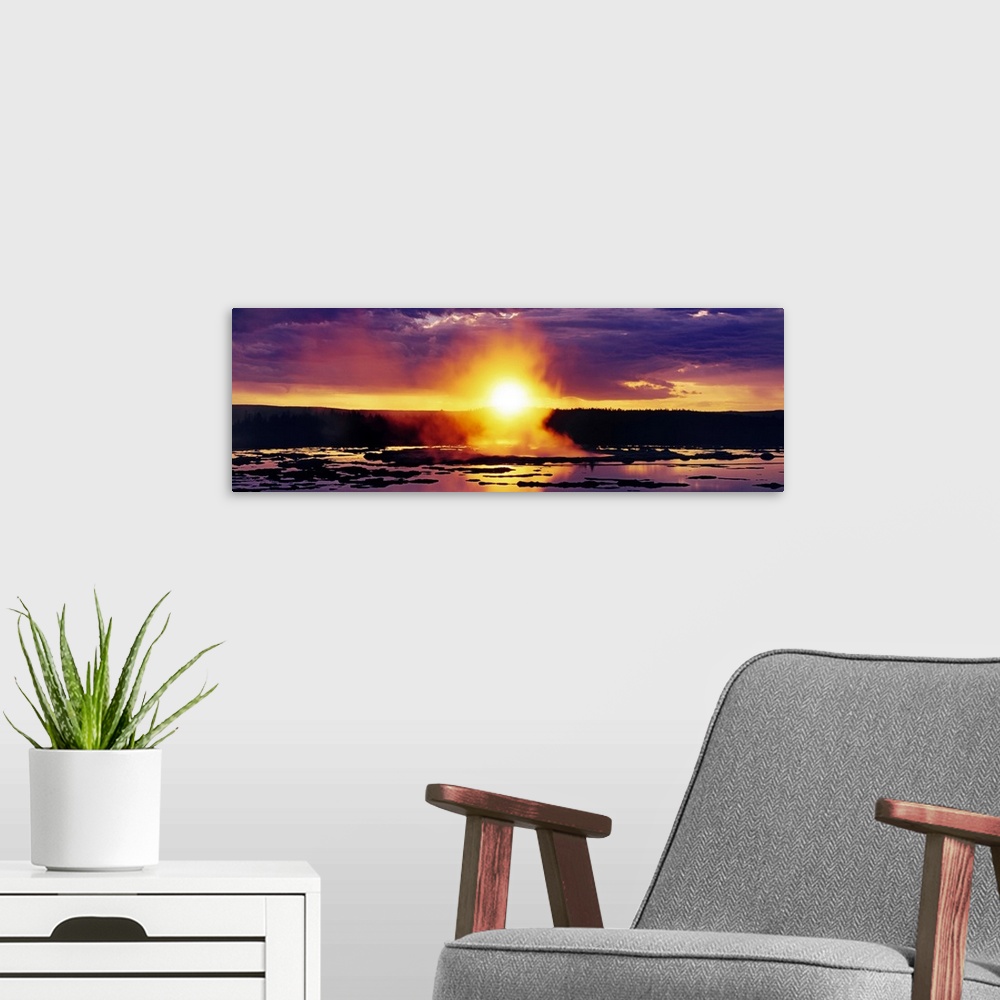 A modern room featuring Wide angle shot of the sun setting over Yellowstone as steam billows off the water below.