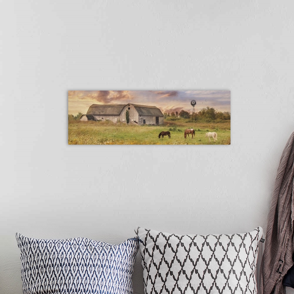 A bohemian room featuring Horses grazing in a field near a large barn in the country.