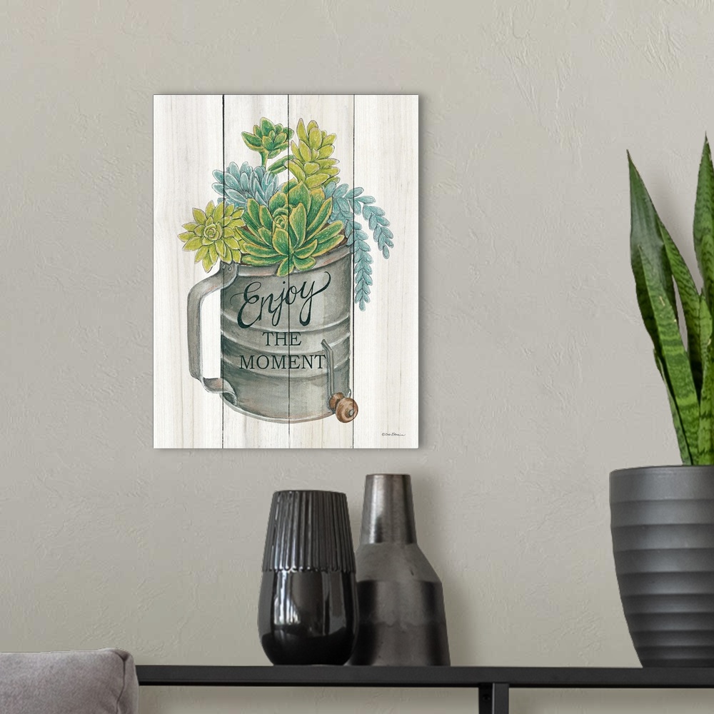 A modern room featuring The words, Enjoy the moment, are placed over an aged flour sifter filled with vibrant succulents ...