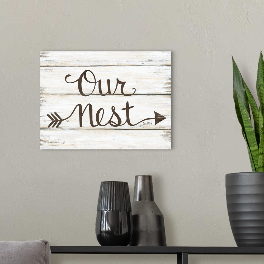 A modern room featuring This decorative artwork features the phrase: our nest, over a distressed wood planks.