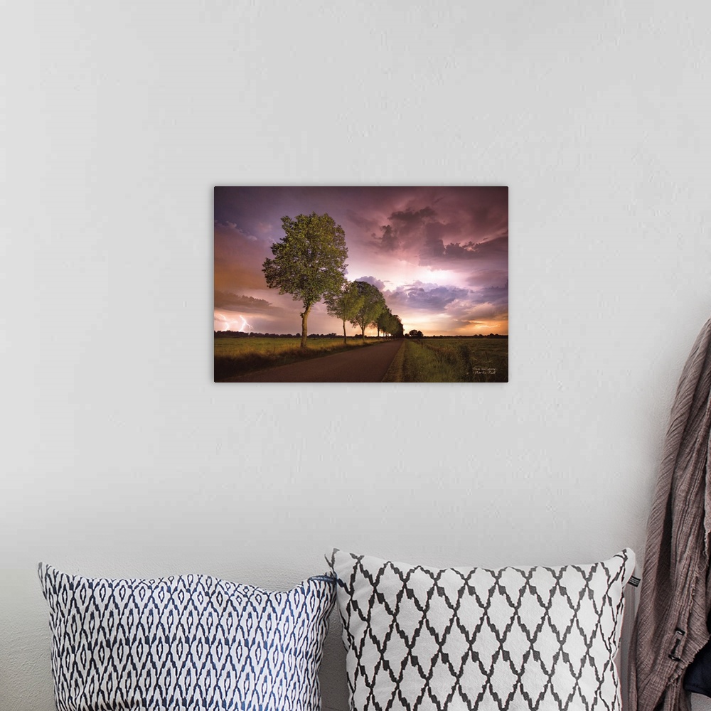 A bohemian room featuring Lightning in the pink clouds over a tree-lined road in the countryside.