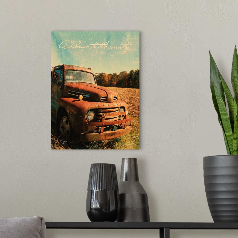 A modern room featuring The words: Welcome to the country, are placed over rusted pick-up truck with distressing throughout.