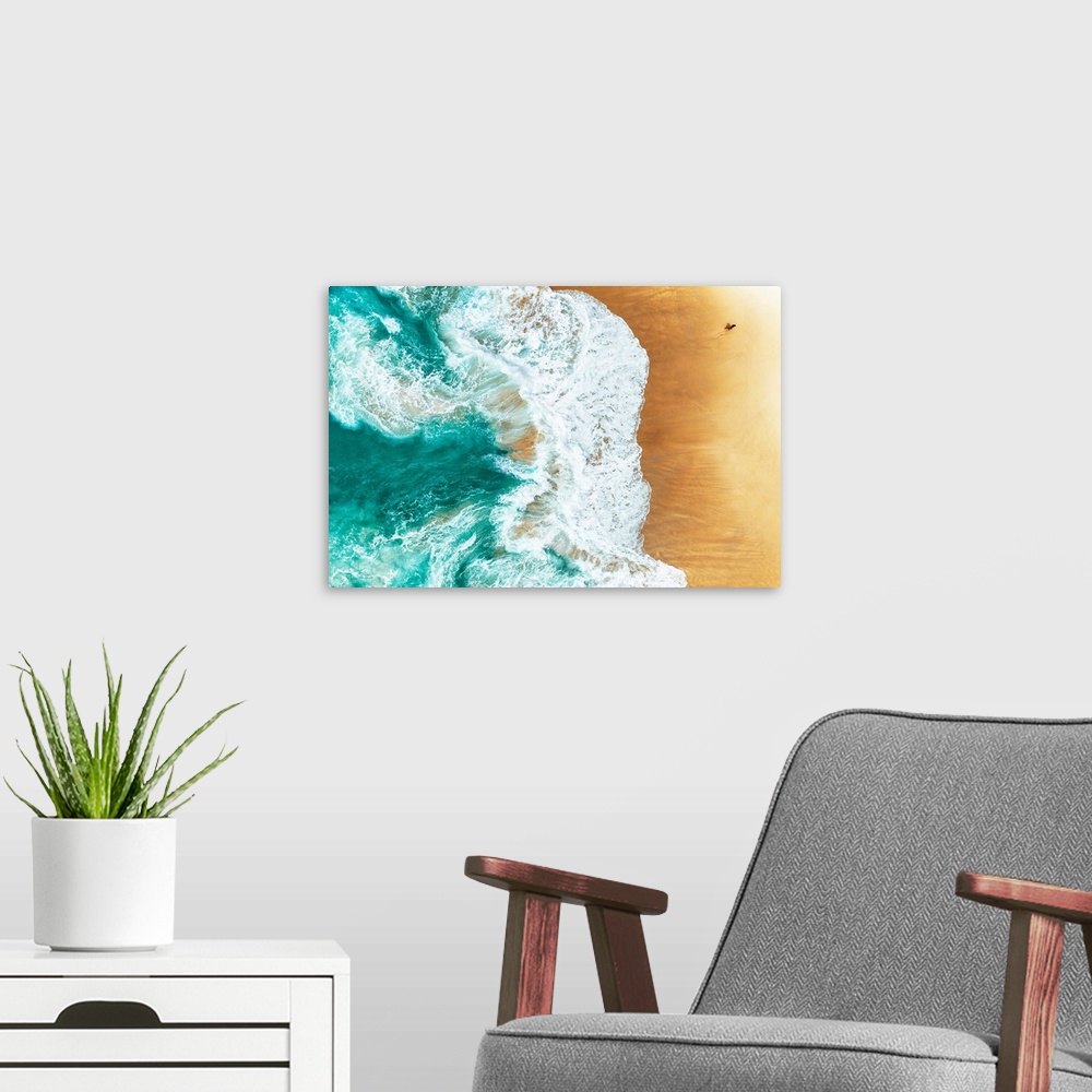 A modern room featuring A stunning overhead aerial photograph of bright turquoise waves crashing onto a sandy beach