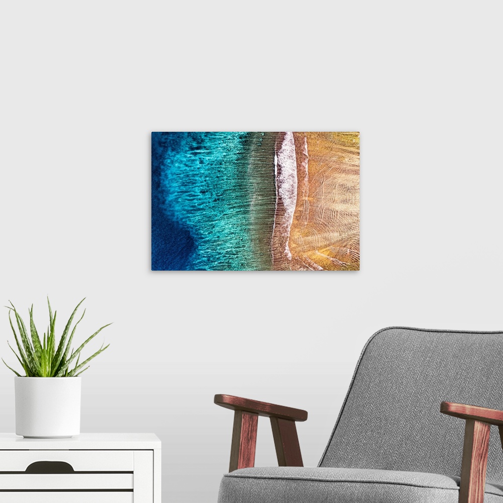 A modern room featuring A stunning overhead aerial photograph of slow waves receding from a sandy beach, it resembles an ...