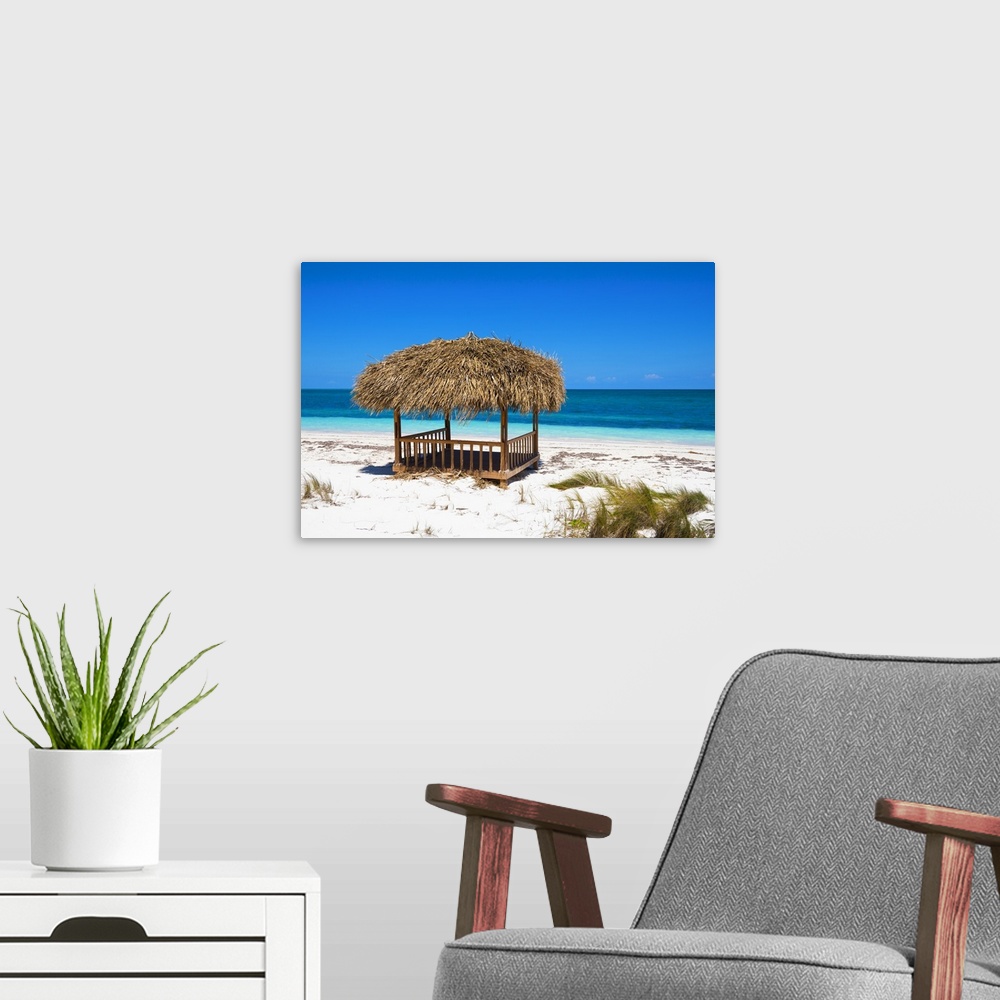 A modern room featuring Landscape photograph of a relaxing cabana on the white sands of a Cuban beach with crystal blue w...
