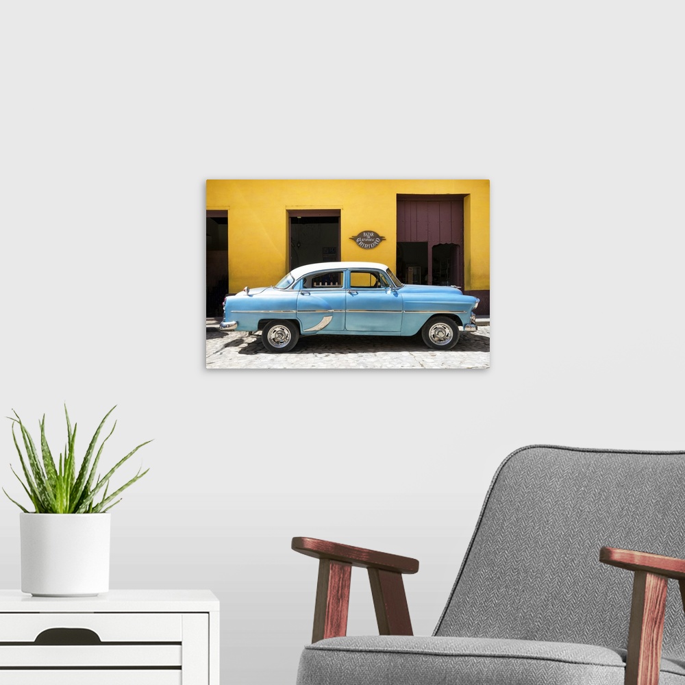 A modern room featuring Photograph of a blue vintage car parked in front of a bright yellow building on a cobblestone road.