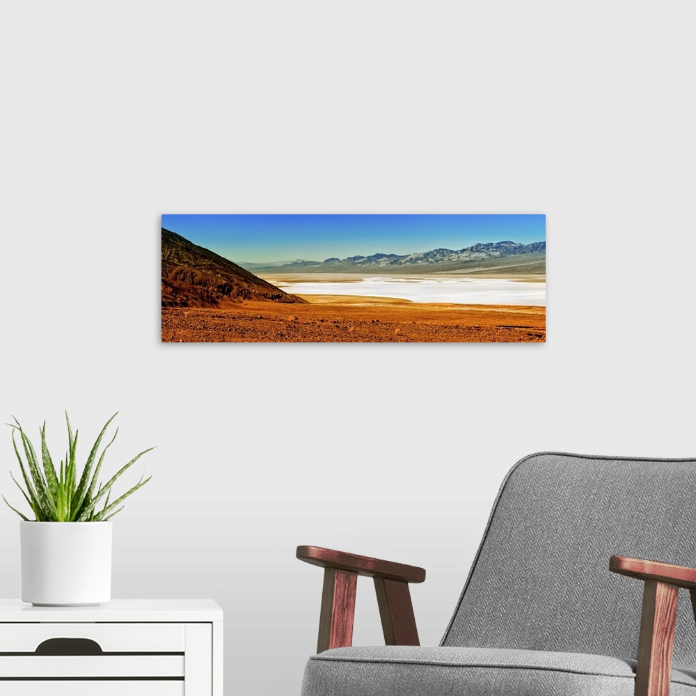 A modern room featuring Photo of the Death Valley desert landscape, a flat plain bordered by low mountains.