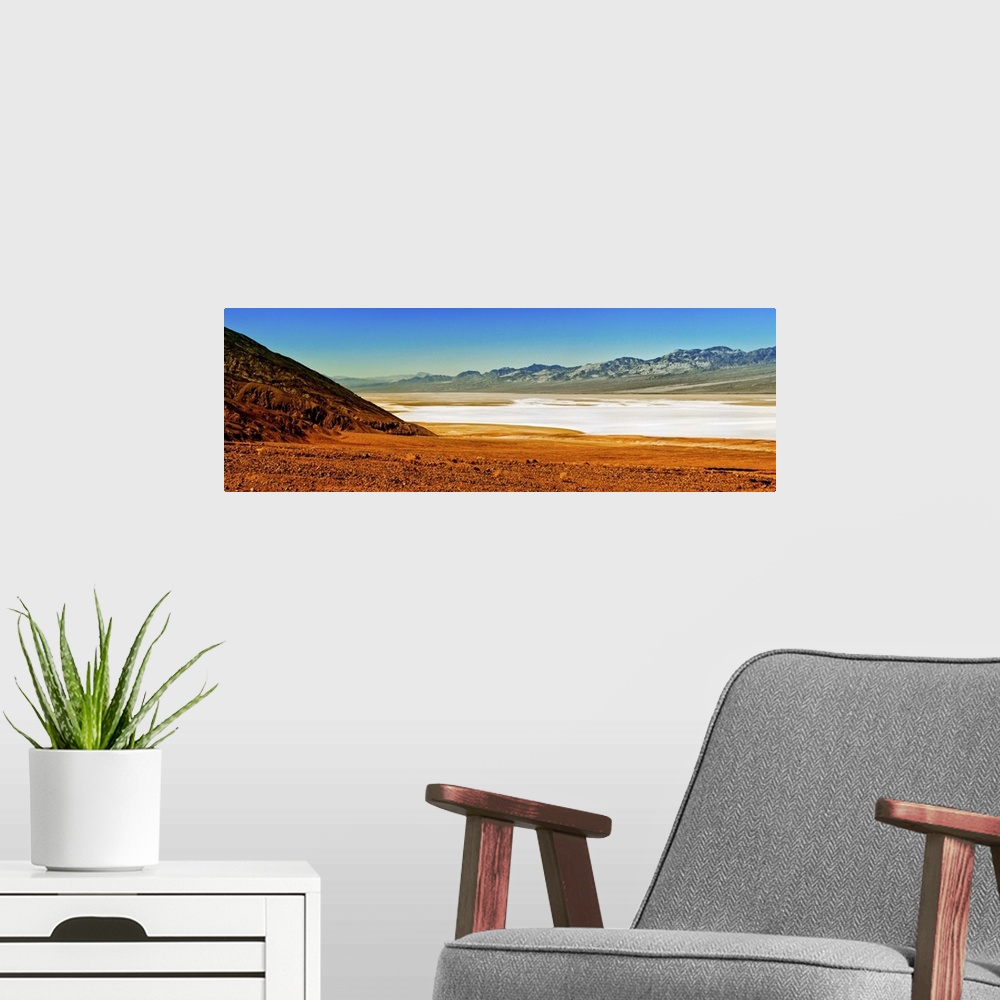 A modern room featuring Photo of the Death Valley desert landscape, a flat plain bordered by low mountains.