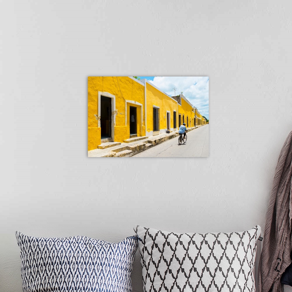 A bohemian room featuring Pphotograph highlighting the yellow buildings in Izamal, Yucat?n, Mexico, with a man in blue ridi...