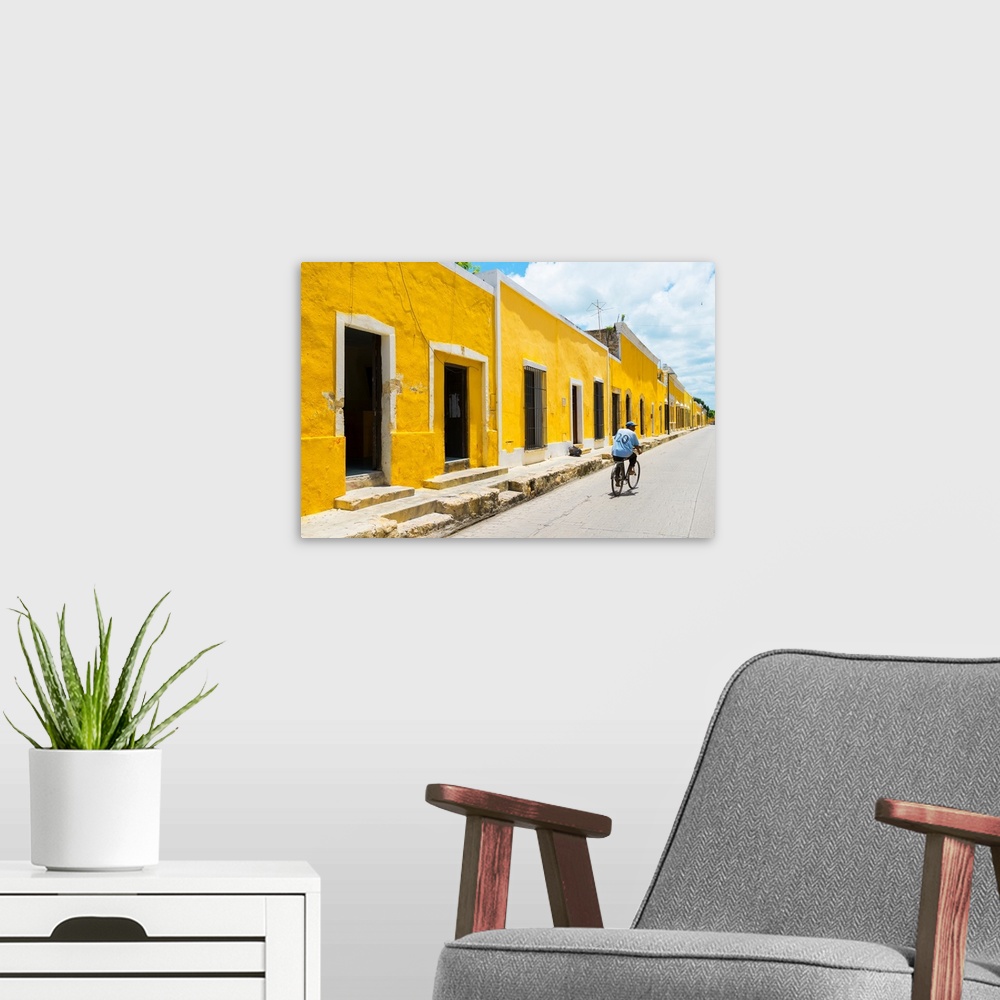 A modern room featuring Pphotograph highlighting the yellow buildings in Izamal, Yucat?n, Mexico, with a man in blue ridi...