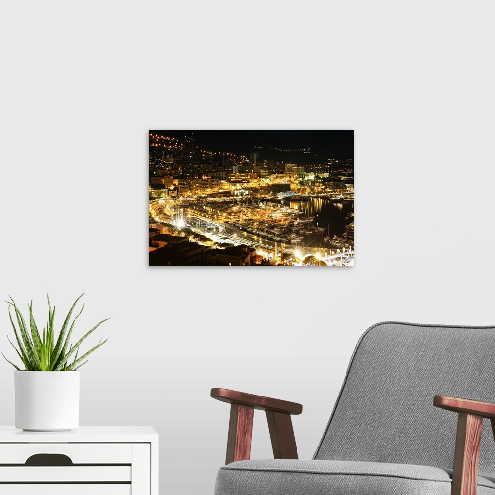A modern room featuring The city of Monaco filled with bright lights in the evening.