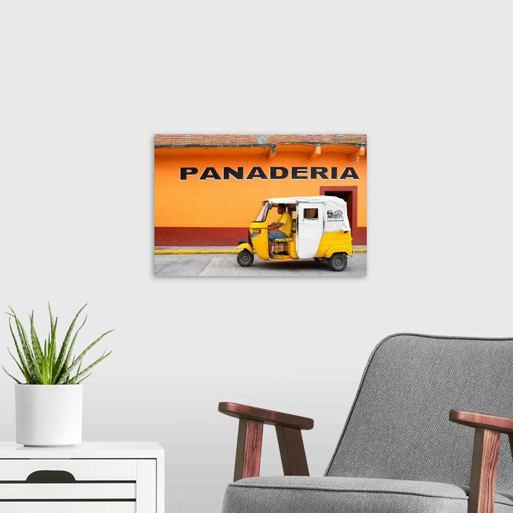 A modern room featuring Photograph of a yellow Tuk Tuk (taxi) driving on the street in front of a bakery with orange exte...