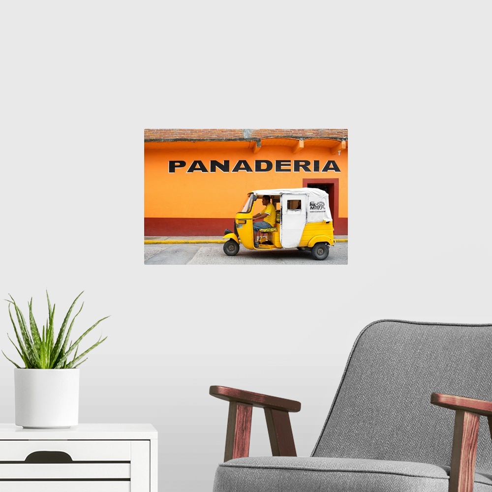 A modern room featuring Photograph of a yellow Tuk Tuk (taxi) driving on the street in front of a bakery with orange exte...