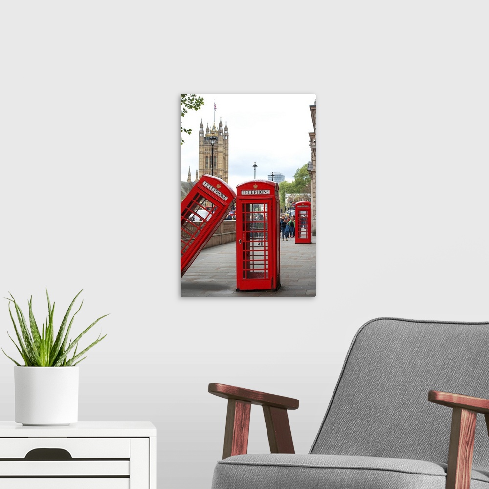A modern room featuring Three red phone booths, one leaning against the other, with the House of Parliament in the backgr...