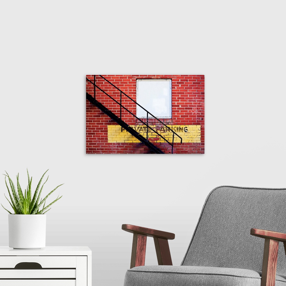 A modern room featuring A notice of private parking is painted on a brick wall with metal fire escape stairs.
