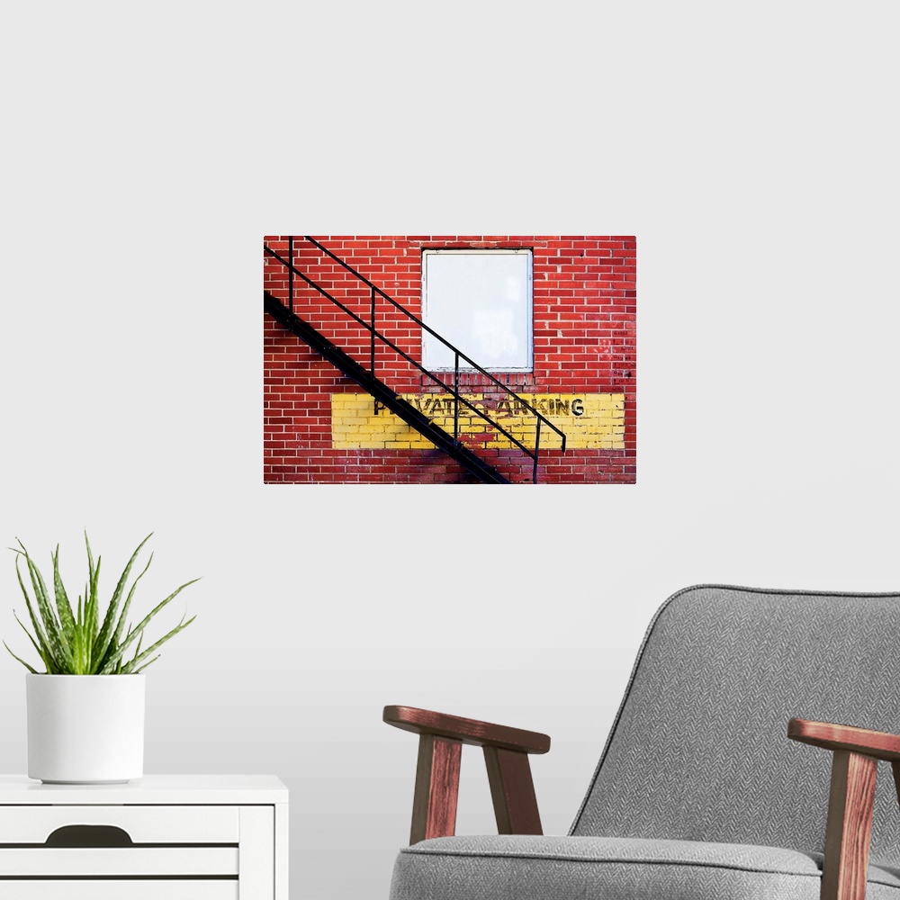 A modern room featuring A notice of private parking is painted on a brick wall with metal fire escape stairs.