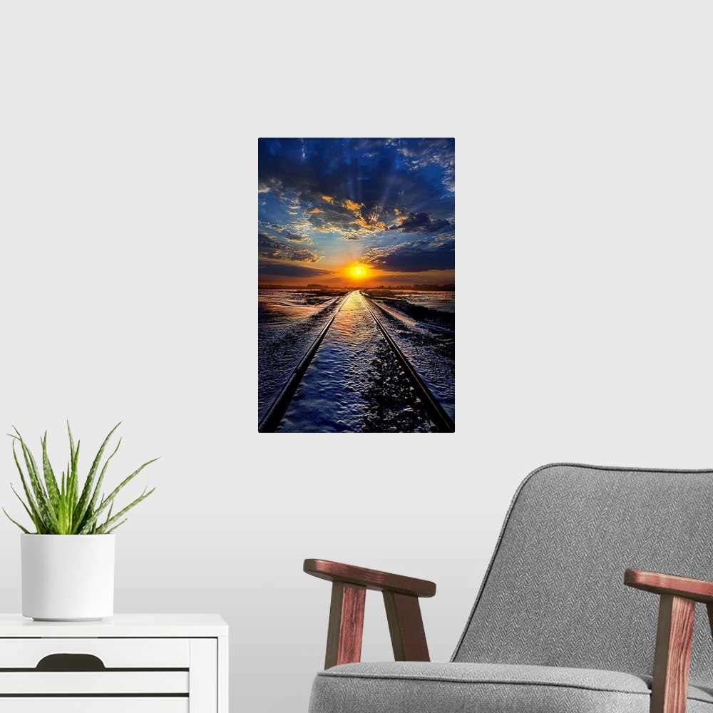 A modern room featuring Railroad tracks leading across a snowy field to the sunset on the horizon, with a cloudy sky.