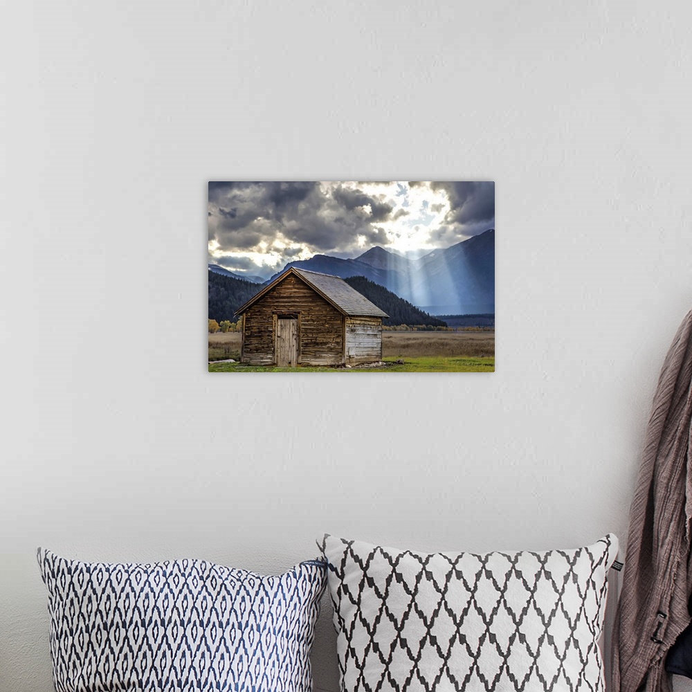 A bohemian room featuring Rays of sunlight shining through the clouds over an old barn in the Grand Teton region, Wyoming.