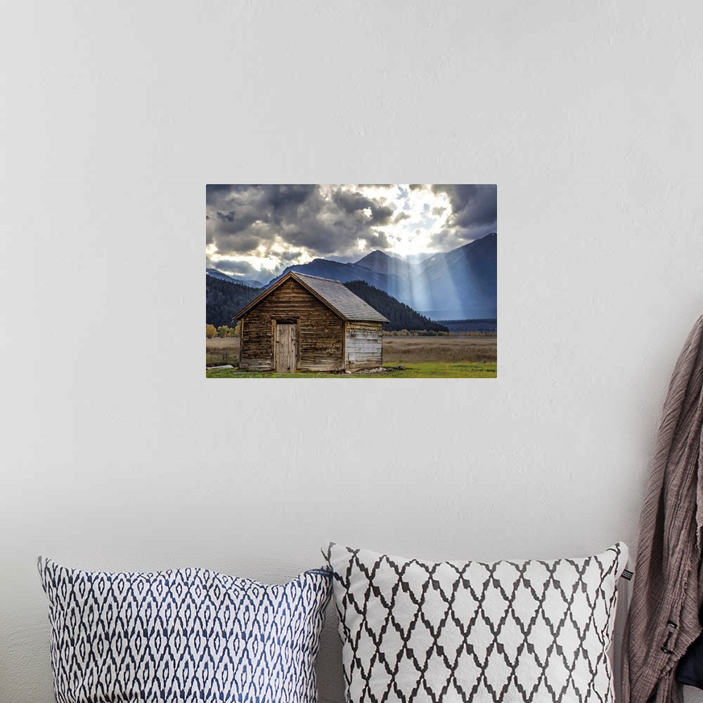 A bohemian room featuring Rays of sunlight shining through the clouds over an old barn in the Grand Teton region, Wyoming.