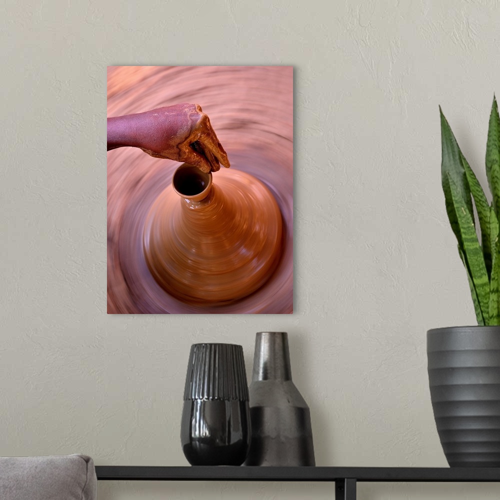 A modern room featuring A potter sculpts the spout of a clay vessel as it spins on a pottery wheel.