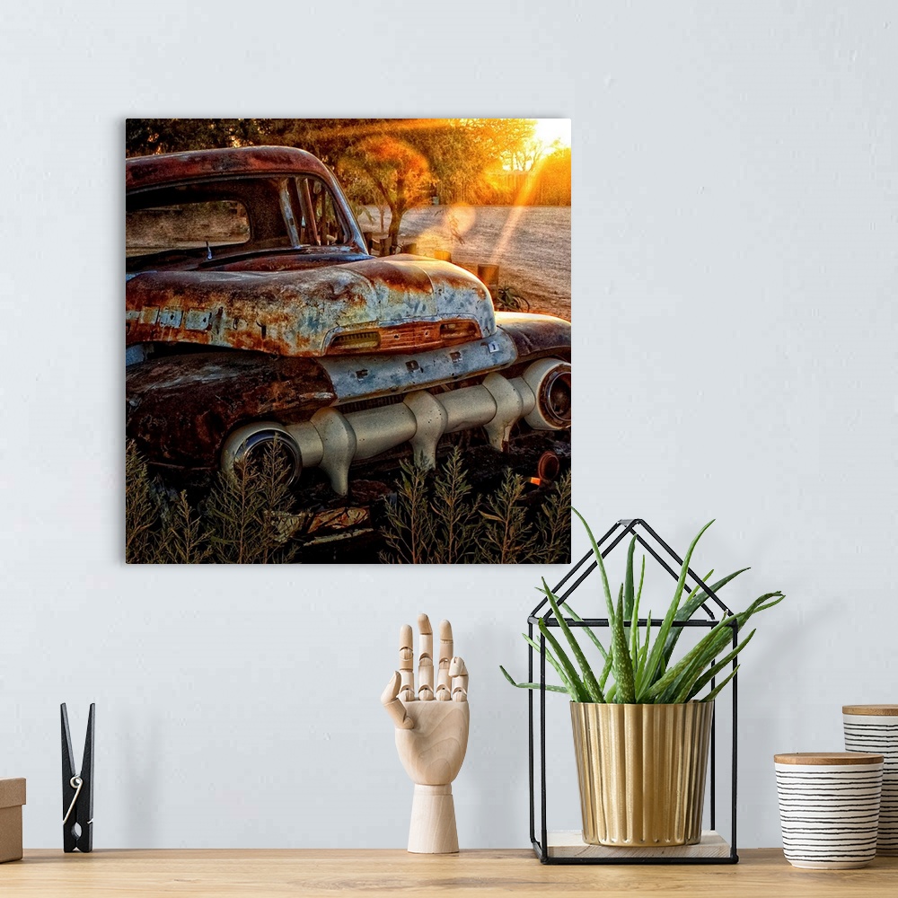 A bohemian room featuring An old abandoned Ford car covered in rust in the sunset.