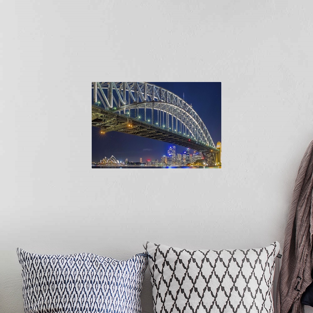 A bohemian room featuring The Sydney harbor skyline lit up in neon lights at night, seen from under a large arcing bridge.