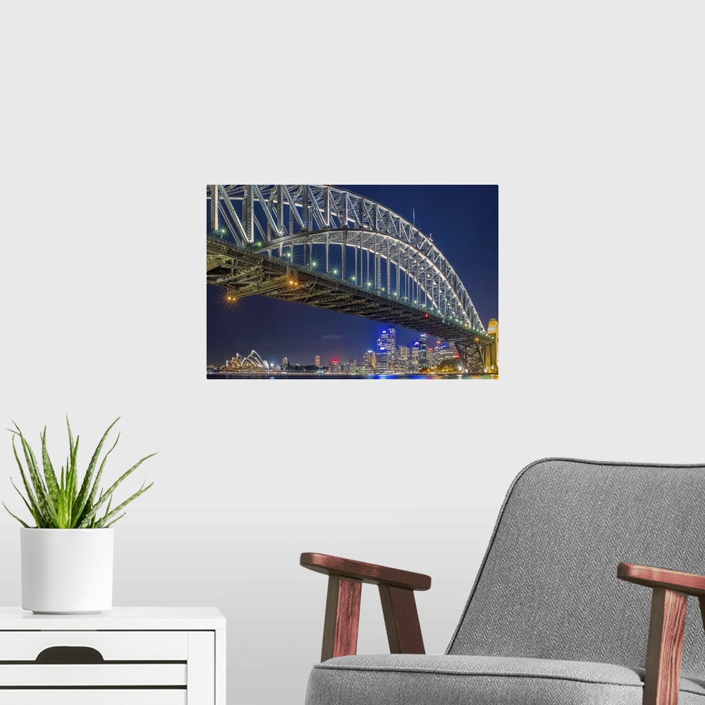 A modern room featuring The Sydney harbor skyline lit up in neon lights at night, seen from under a large arcing bridge.