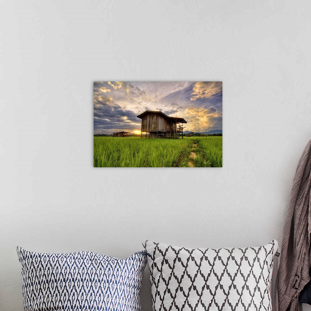 A bohemian room featuring An old wooden building in a field under a colorful sunset sky.