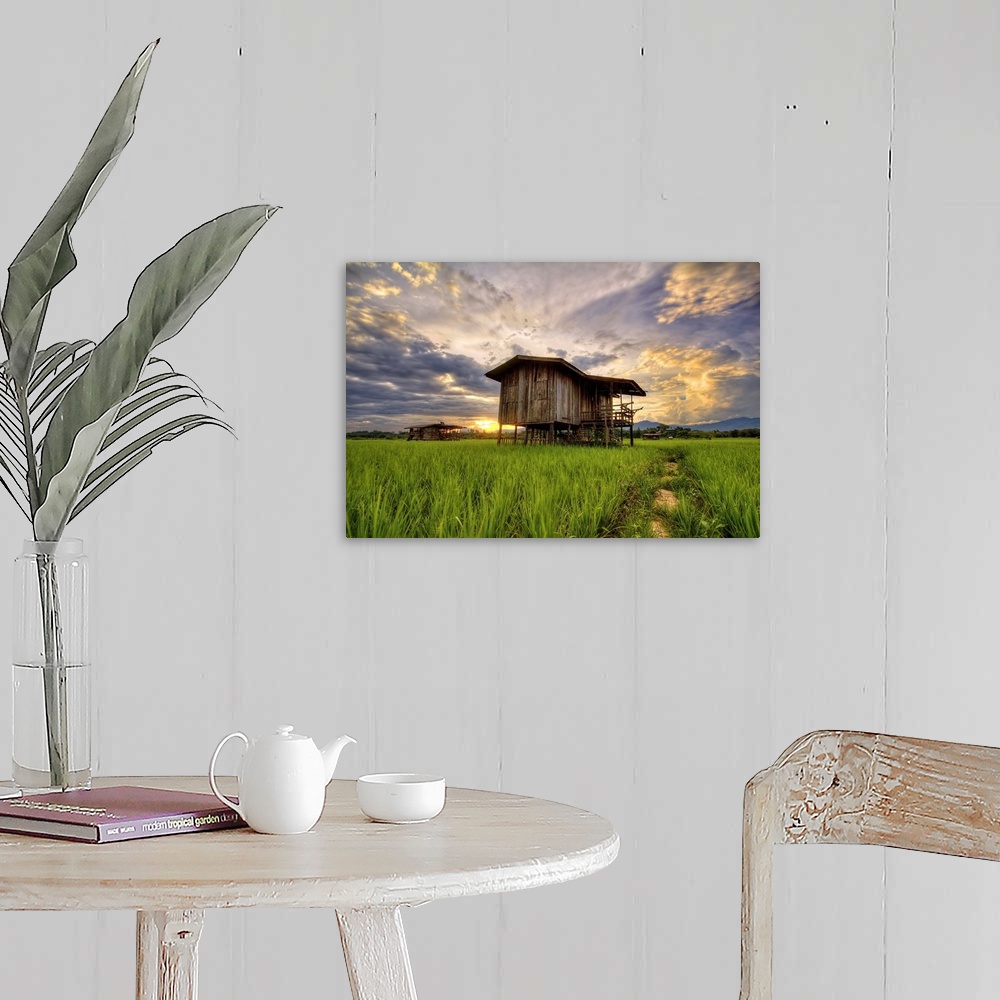 A farmhouse room featuring An old wooden building in a field under a colorful sunset sky.