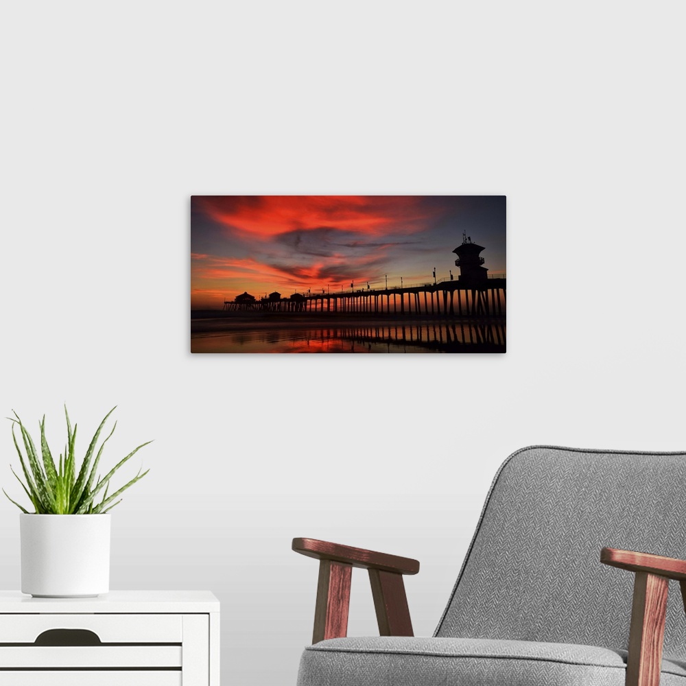 A modern room featuring Huntington Beach Pier, California, at sunset, with bright red clouds above.