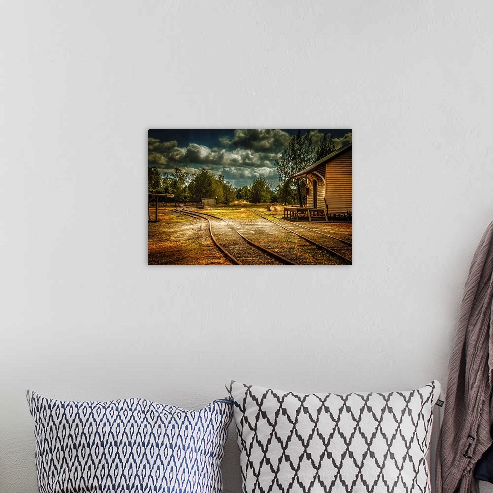 A bohemian room featuring Train tracks through a village under dark clouds.