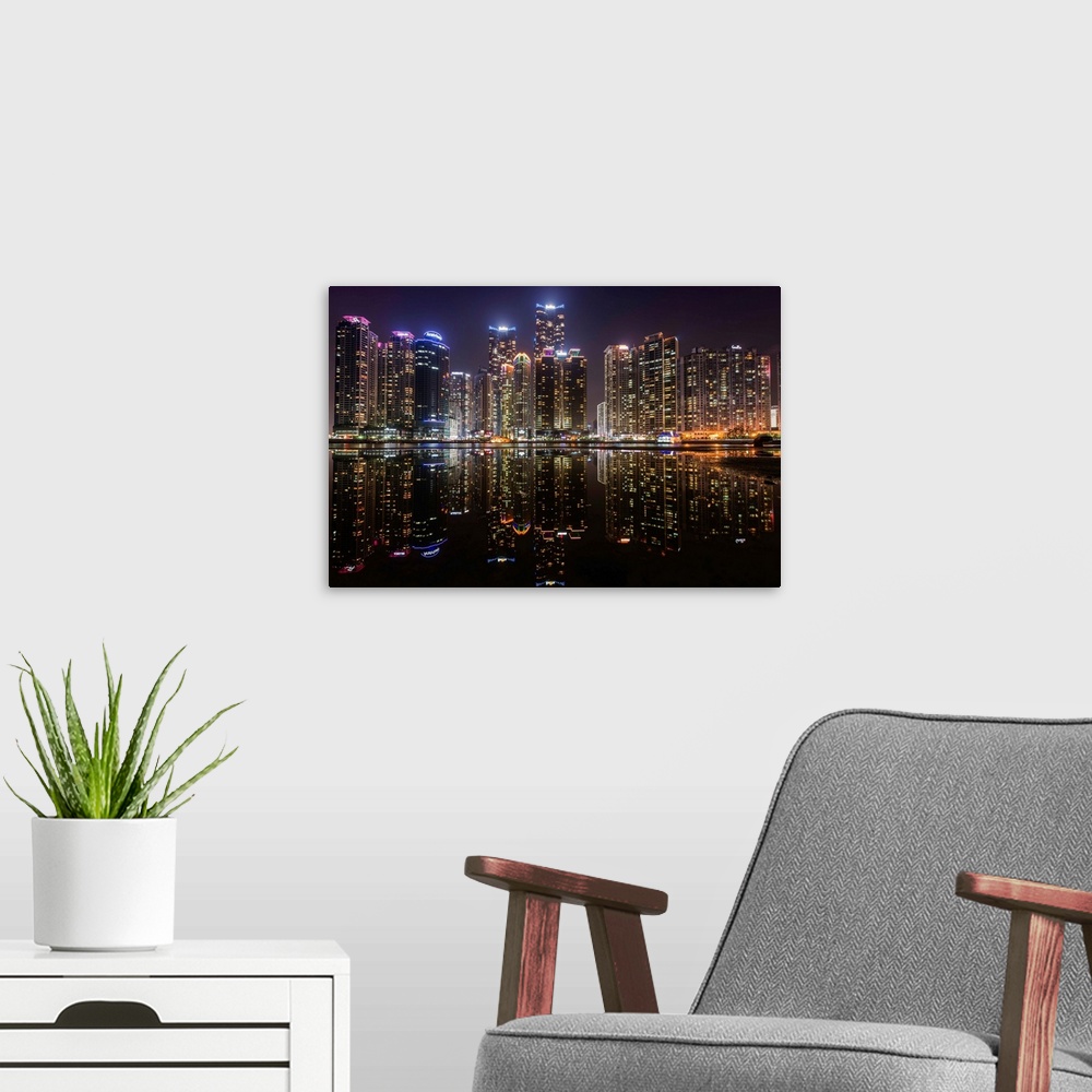 A modern room featuring The city of Busan, South Korea, lit up at night, reflected in the water.
