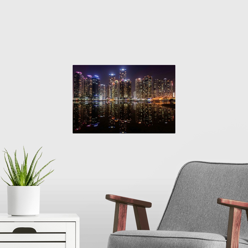 A modern room featuring The city of Busan, South Korea, lit up at night, reflected in the water.