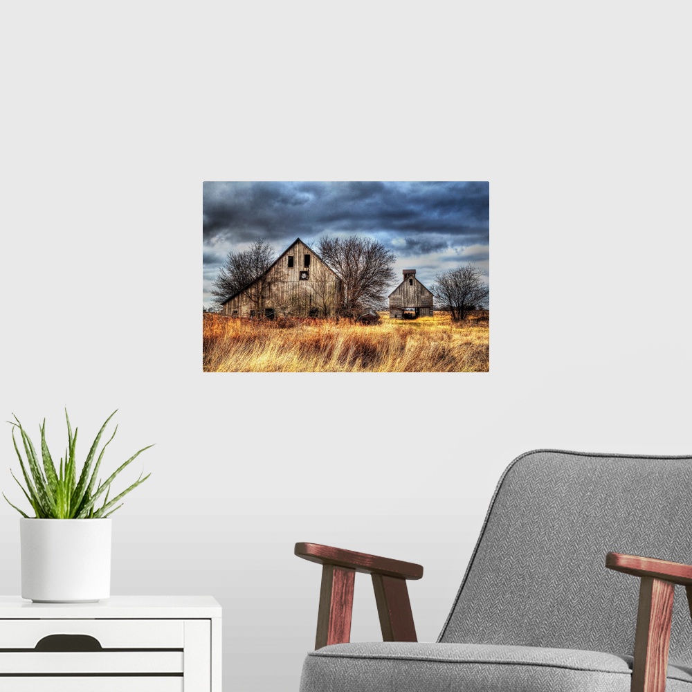 A modern room featuring An image of two farm outbuildings under a dark and stormy sky.