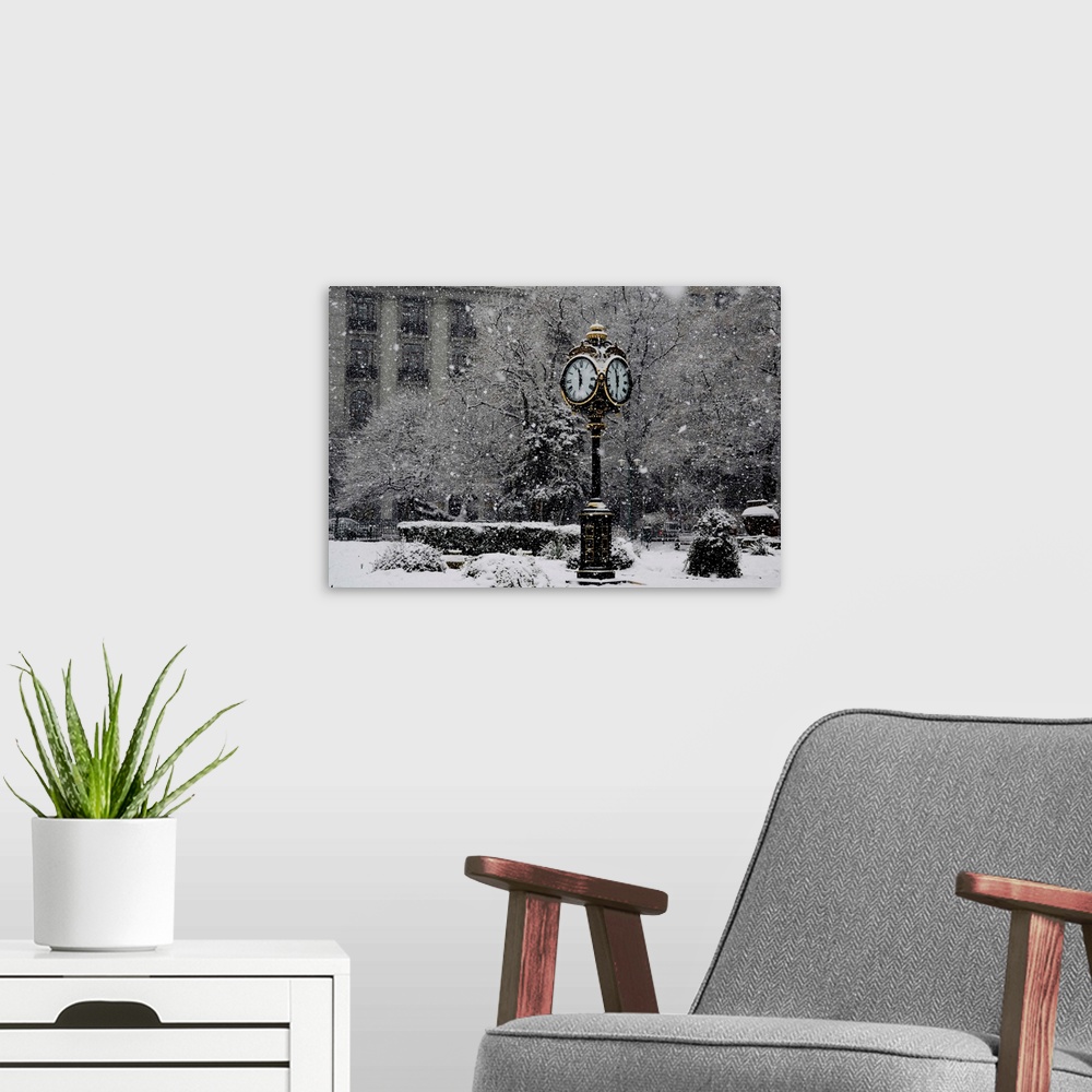 A modern room featuring A large clock standing in a park while snow falls around it.